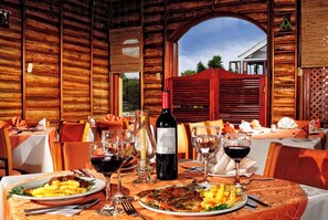 A wooden dining area with tables set for a meal, including plates of food and wine glasses. - Hotel El Lago (Paipa)