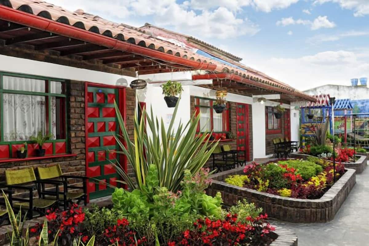 A building with a red and white facade, outdoor seating, and a garden with various plants.