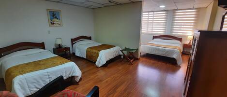 A hotel room with three beds, wooden flooring, and a ceiling with recessed lighting.