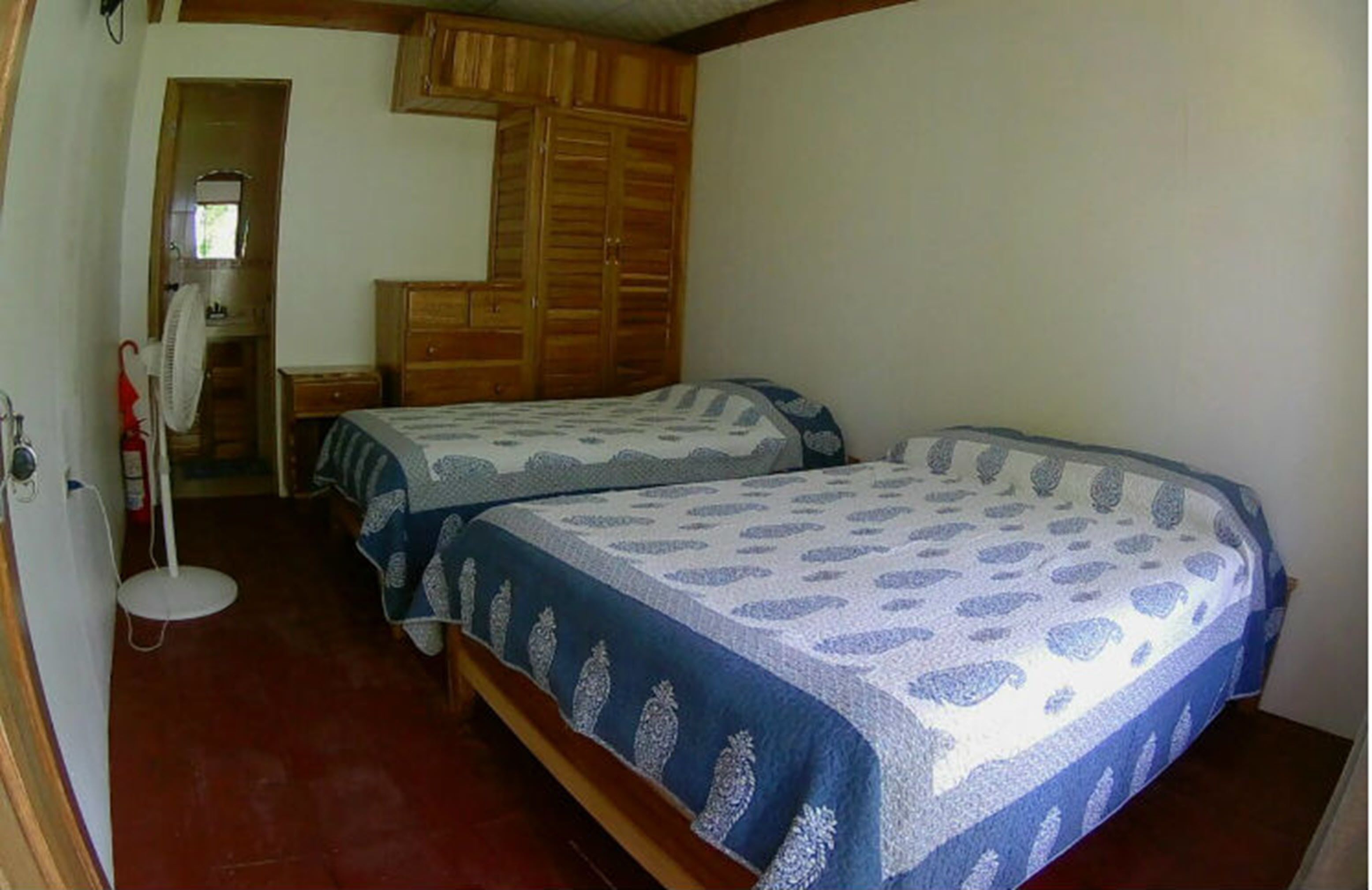 Un dormitorio con dos camas, un armario de madera y un escritorio pequeño con una silla.