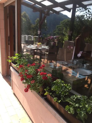 Et udendørs spiseområde med borde og stole, omgivet af krukker med planter og blomster.