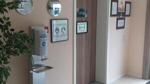 Ein Empfangsbereich mit Handdesinfenspender, informativen Schildern in Rahmen und einem Spiegel an der Wand.