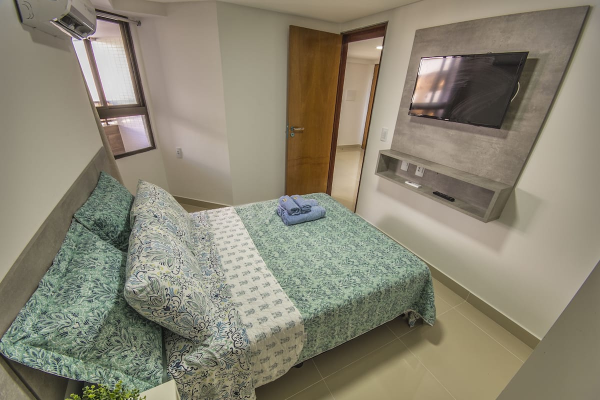 A bedroom with a bed, a TV mounted on the wall, and a window.