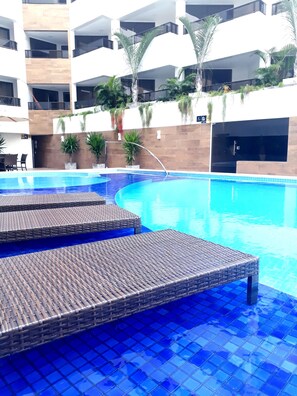 Une piscine aux carreaux bleus et des fauteuils de relaxation en osier.