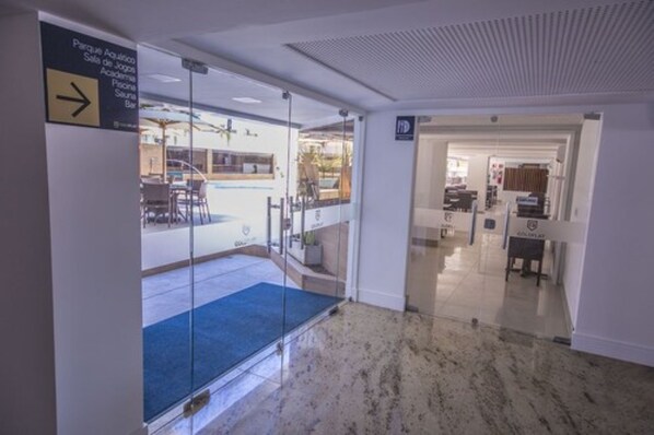 A hotel lobby with a glass partition, a reception desk, and a sign indicating the direction to the aquatic park.
