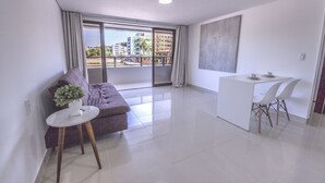 A modern living room with a sofa, a small table with a plant, and a dining area with a white table and chairs. - GOLDFLAT Cabo Branco by Penareia.tur.br (João Pessoa)