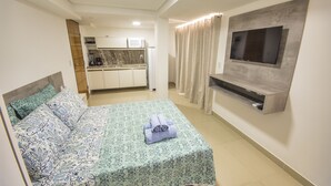 A bedroom with a bed, a TV mounted on the wall, and a kitchen area in the background. - GOLDFLAT Cabo Branco by Penareia.tur.br (João Pessoa)