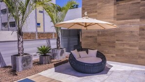 A modern outdoor seating area with a round, woven chair and a large umbrella. - GOLDFLAT Cabo Branco by Penareia.tur.br (João Pessoa)