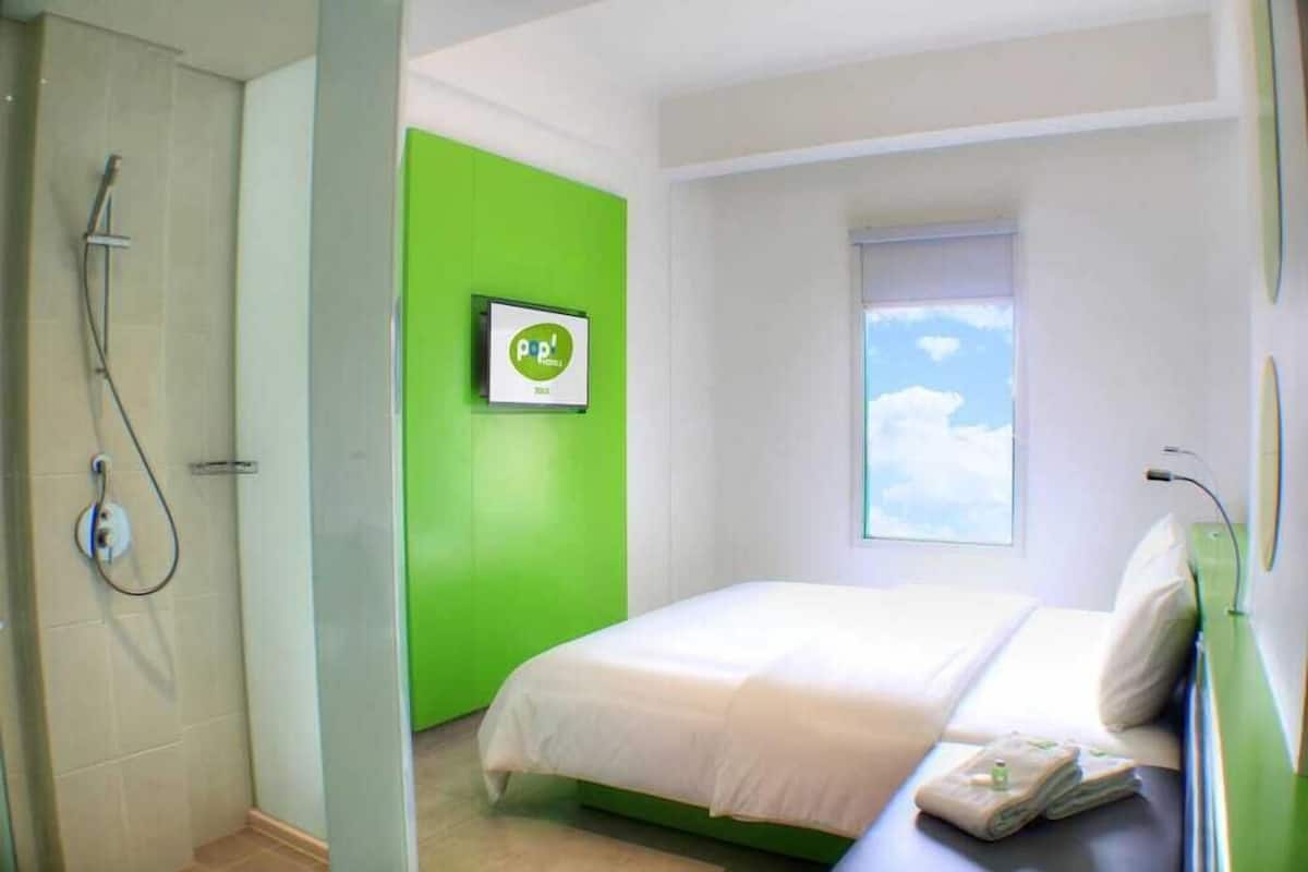 A hotel room with a bed, a green accent wall, a window with a view, and a shower area.