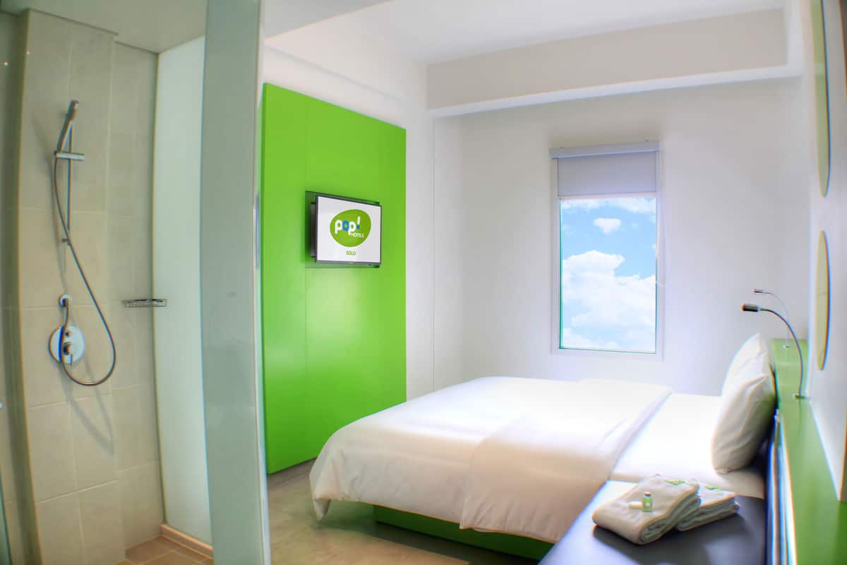 A modern hotel room with a bed, a green accent wall, a window with a view, and a shower.