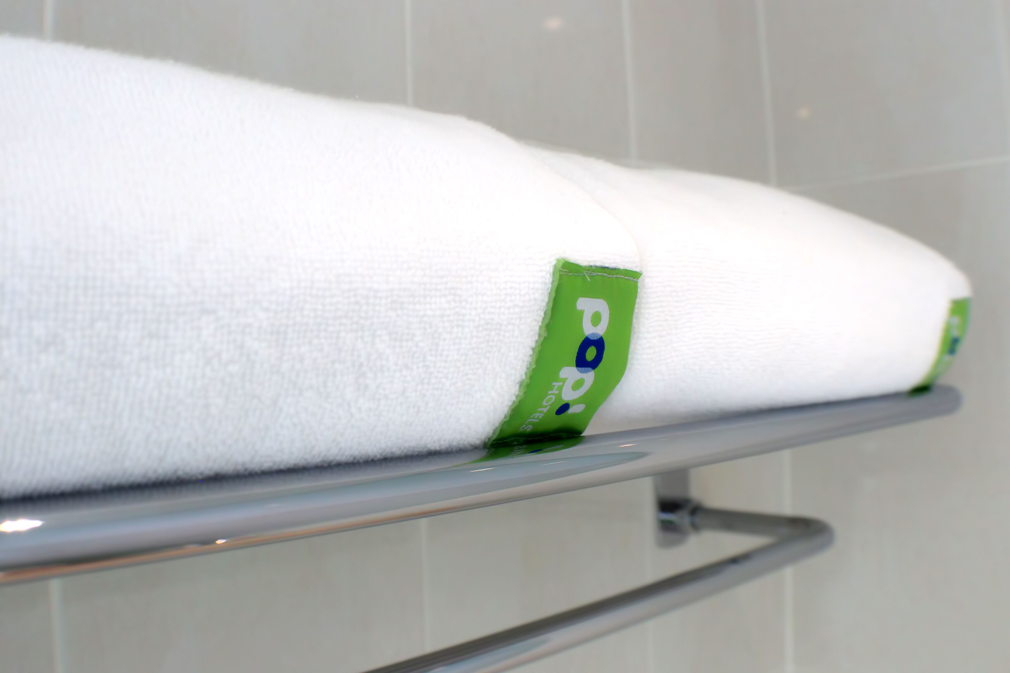 Toalla blanca con etiqueta verde sobre un perchero metálico en un baño.