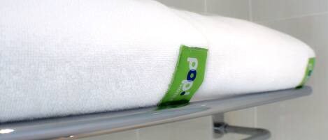 Toalla blanca con etiqueta verde sobre un perchero metálico en un baño.