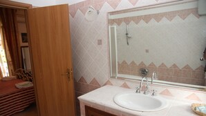 A bathroom with a sink, mirror, shower, and wooden door. - Villa Catalano (Paola)