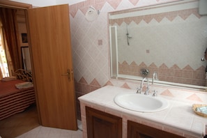 A bathroom with a sink, mirror, shower, and wooden door. - Villa Catalano (Paola)