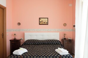A bedroom with a bed, two nightstands, a painting on the wall, and a door. - Villa Catalano (Paola)