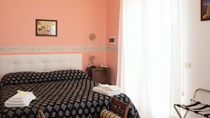 A bedroom with a patterned bedspread, a bedside table with a lamp, and a framed picture on the wall. - Villa Catalano (Paola)