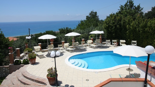 A swimming pool with lounge chairs and umbrellas, surrounded by potted plants and a view of the sea. - Villa Catalano (Paola)