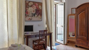 Ein Hotelzimmer mit Bett, Schreibtisch inklusive Computer, Stuhl, Kleiderschrank und einem Gemälde an der Wand.
