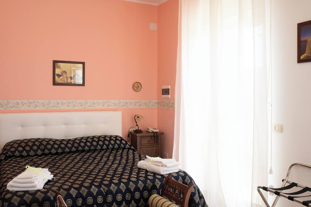 A bedroom with a patterned bedspread, a bedside table with a lamp, and a framed picture on the wall.