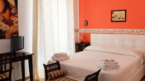 A hotel room with a bed, a desk with a computer, a chair, and a window with curtains. - Villa Catalano (Paola)