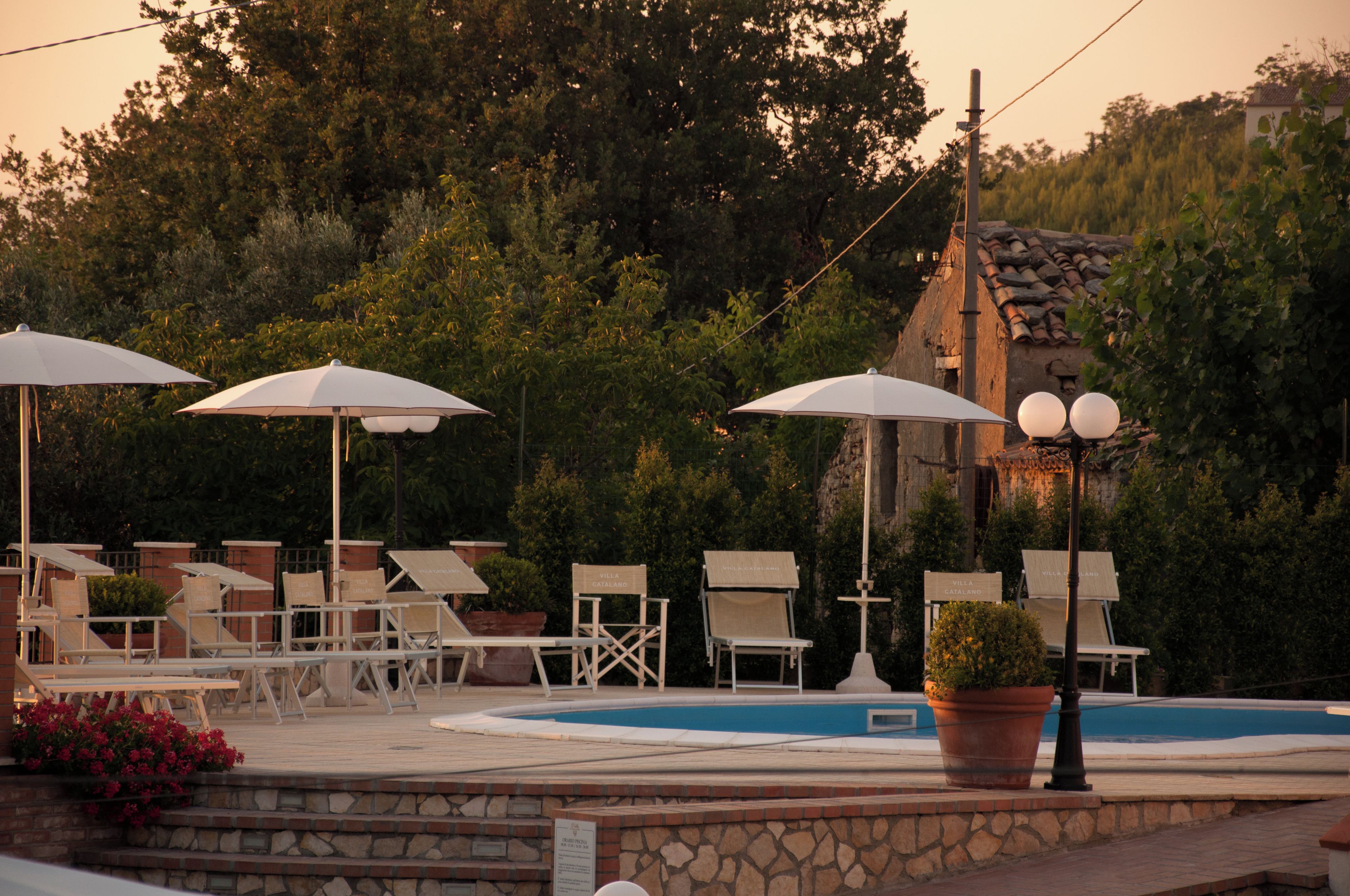 Zona de piscina con sillones y sombrillas, rodeada de vegetación y un muro de piedra.