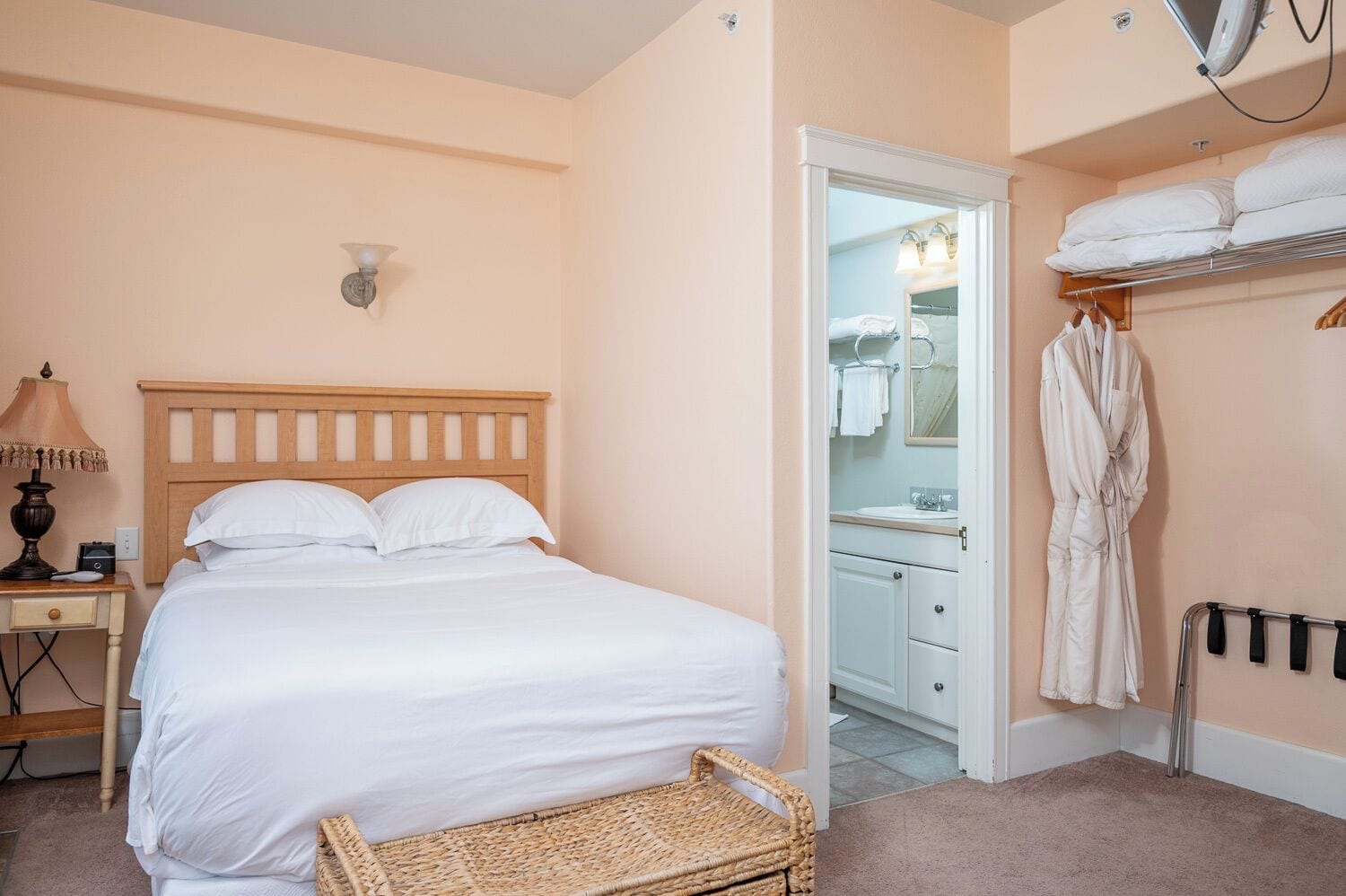 A bedroom with a bed, bedside table, lamp, and a wicker basket.