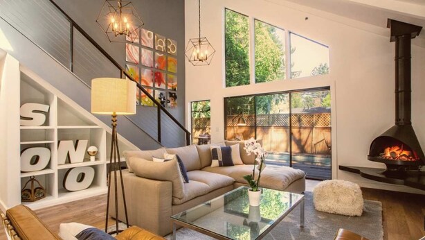 Un salon moderne avec un canapé, une table basse et une cheminée. On y trouve un escalier agrémenté d’un mur décoratif et d’une grande fenêtre.