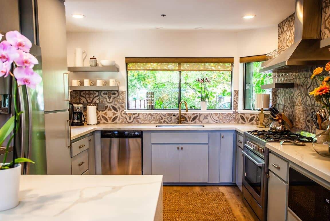 A modern kitchen with a large window, built-in appliances, and decorative tiles.