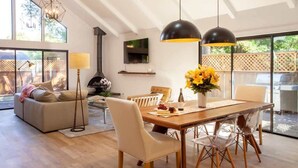 Un salon spacieux avec une table à manger en bois, des chaises transparentes, un canapé et un téléviseur fixé au mur.