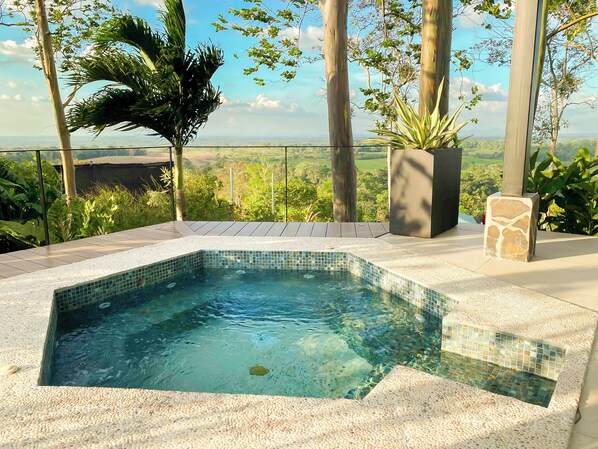Vista despejada de una piscina con borde de azulejos, rodeada por un suelo de guijarros, con vistas al paisaje y árboles al fondo.