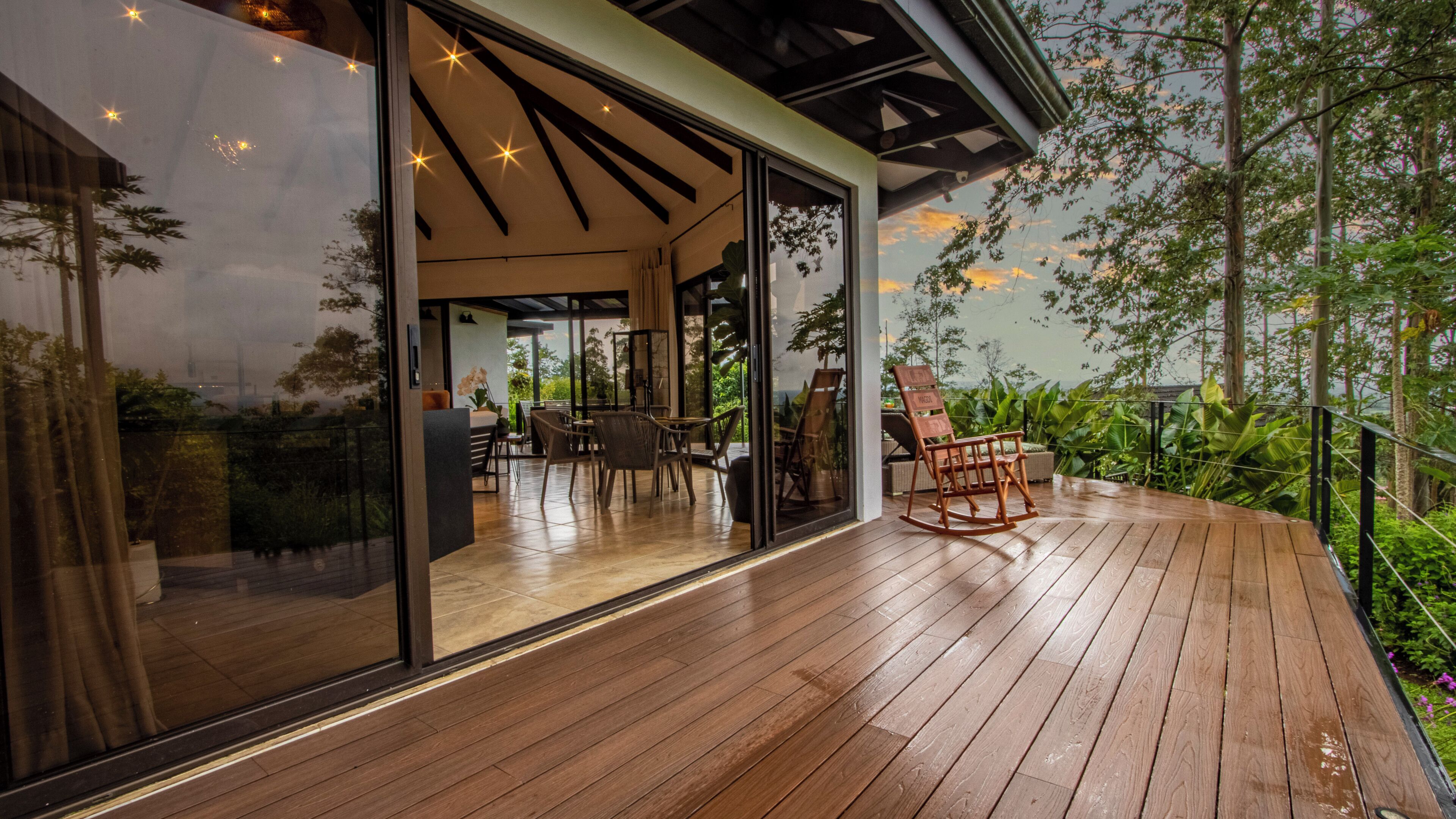 A wooden deck with a glass door leading to an indoor seating area with tables and chairs.