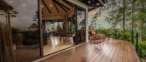 A wooden deck with a glass door leading to an indoor seating area with tables and chairs.
