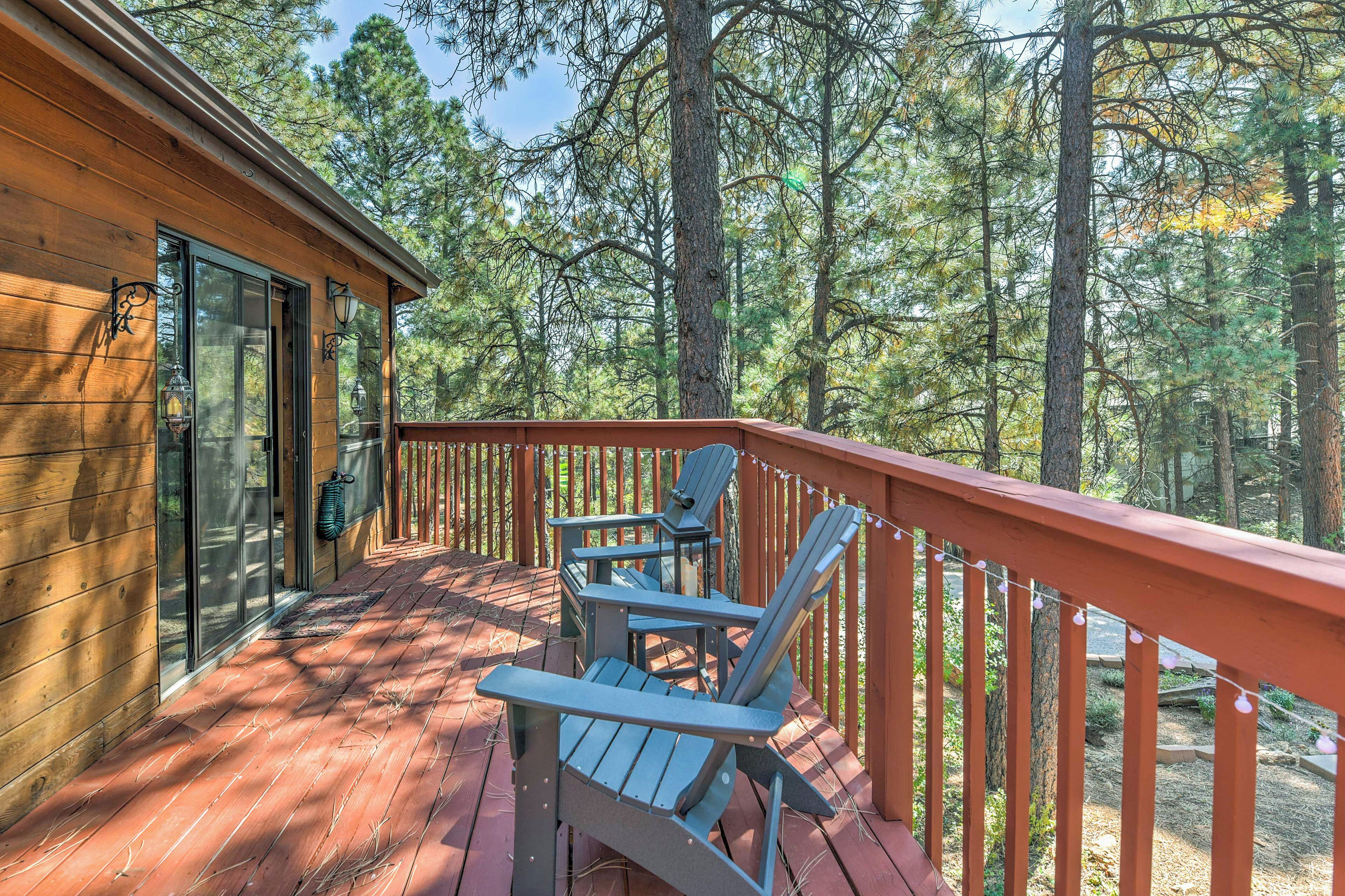 A wooden deck with Adirondack chairs and a red railing, surrounded by trees.