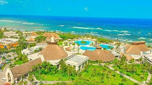 A resort with multiple thatched-roof buildings, a central swimming pool, and a view of the ocean. - Luxury Home Riviera Maya Bahia Principe 5 Star Resort Pool Jacuzzis Beach Access (Akumal)