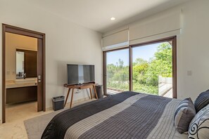 Ein modernes Schlafzimmer mit einem großen Bett, einem Fernseher und einem Balkon mit Blick auf Grünflächen.