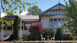 A two-story house with a stone foundation, a blue and white exterior, and a small garden with a table and chairs.