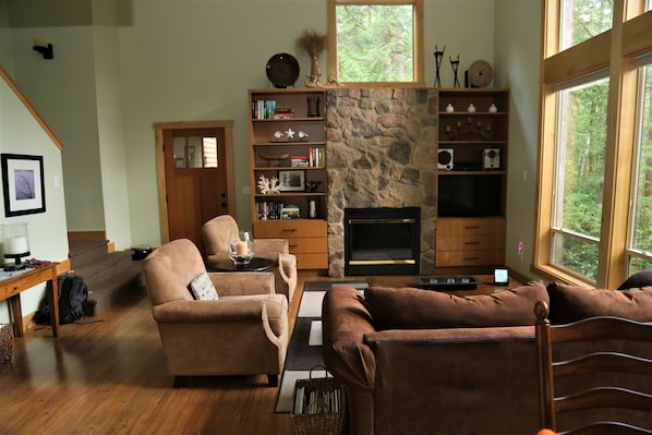 A cozy living room with a stone fireplace, wooden furniture, and a bookshelf.