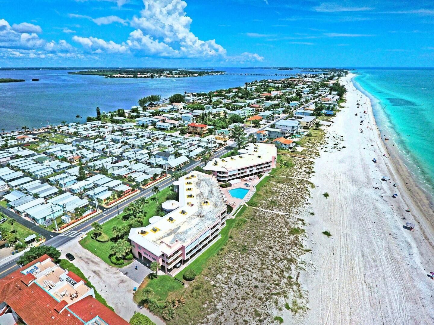 An aerial view of a coastal resort with multiple buildings, a beach, and a clear blue sky.