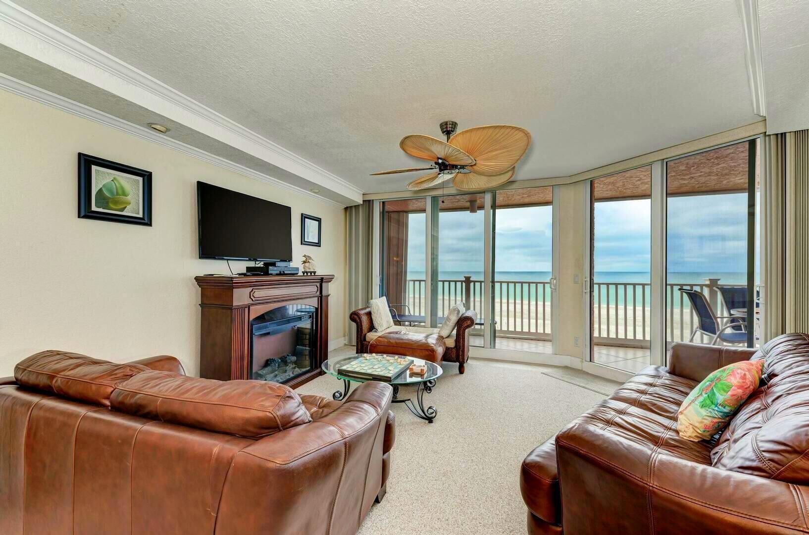 Amplia sala de estar con sofás de cuero, chimenea, televisor y un gran ventanal con vista a la playa.