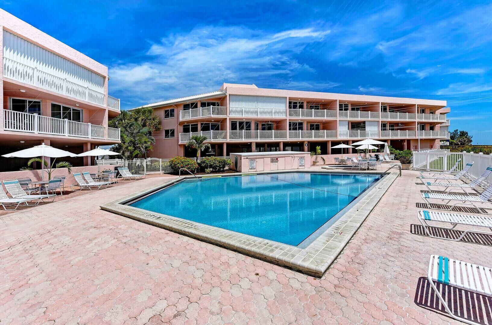 Un hotel con piscina, varios balcones y sillones de sol.