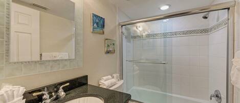 Baño con lavamanos grande, espejo y ducha con mampara de vidrio.