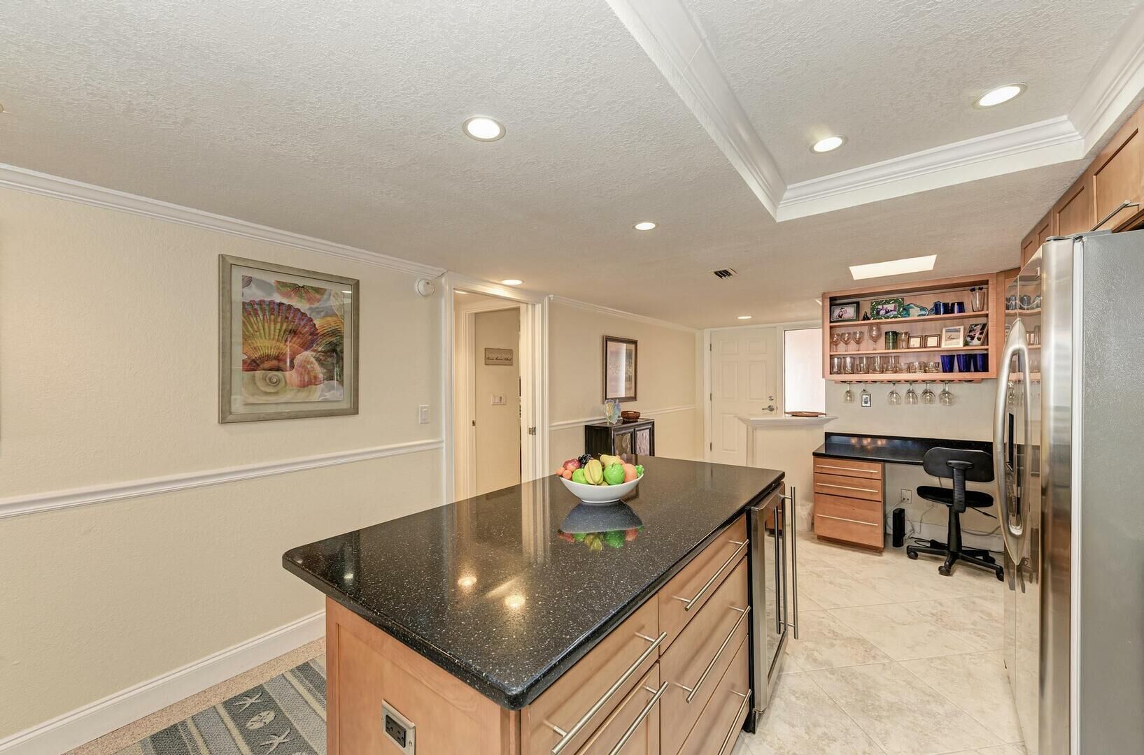 A kitchen with a granite countertop, wooden cabinets, a refrigerator, and a dining area with a chair.