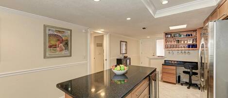 A kitchen with a granite countertop, wooden cabinets, a refrigerator, and a dining area with a chair.