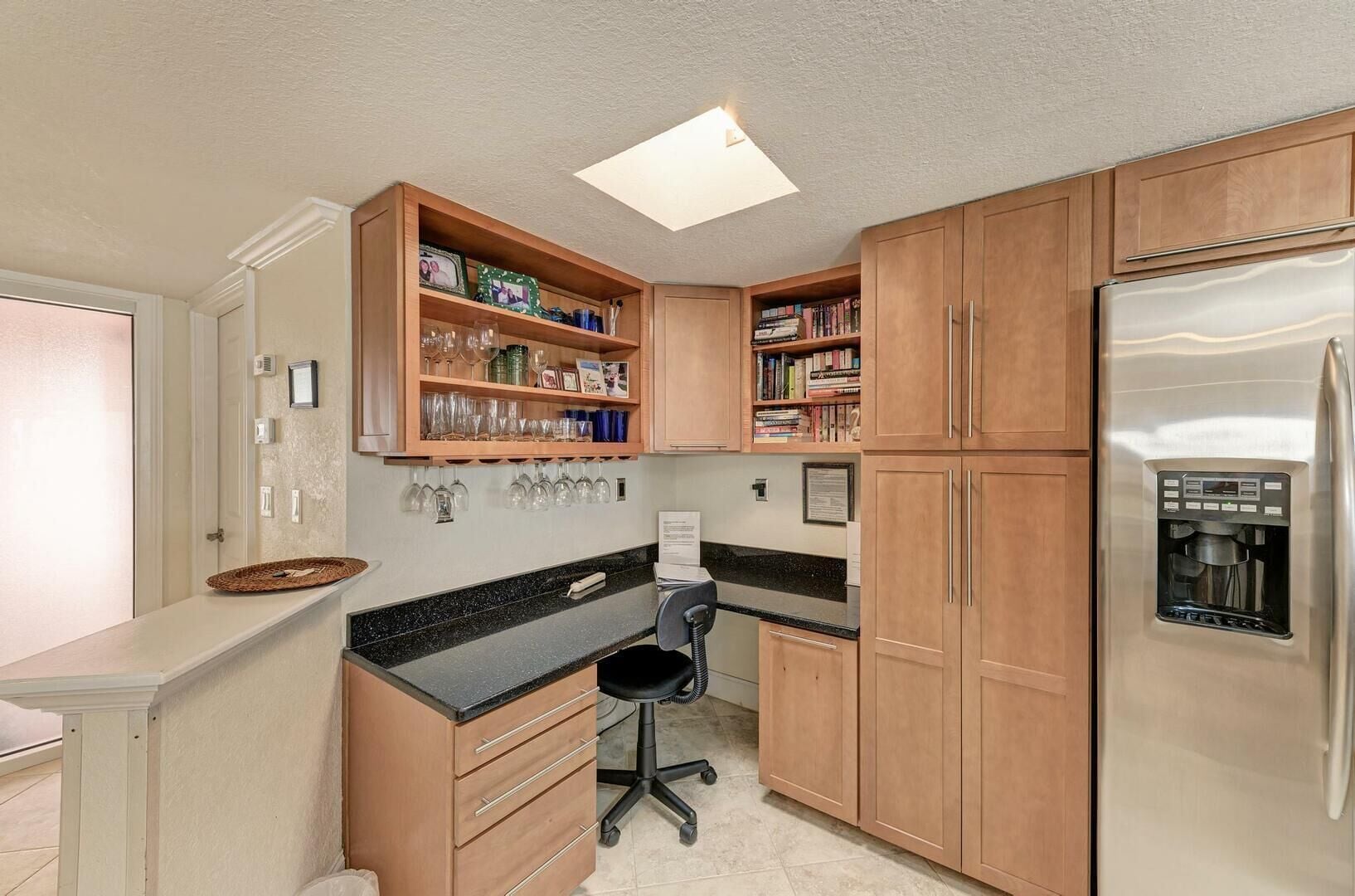 A kitchen with wooden cabinets, a black countertop, a stainless steel refrigerator, and a built-in water dispenser.