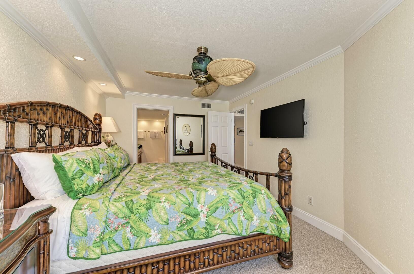 A bedroom with a bed, a ceiling fan, a TV, and a door leading to a bathroom.