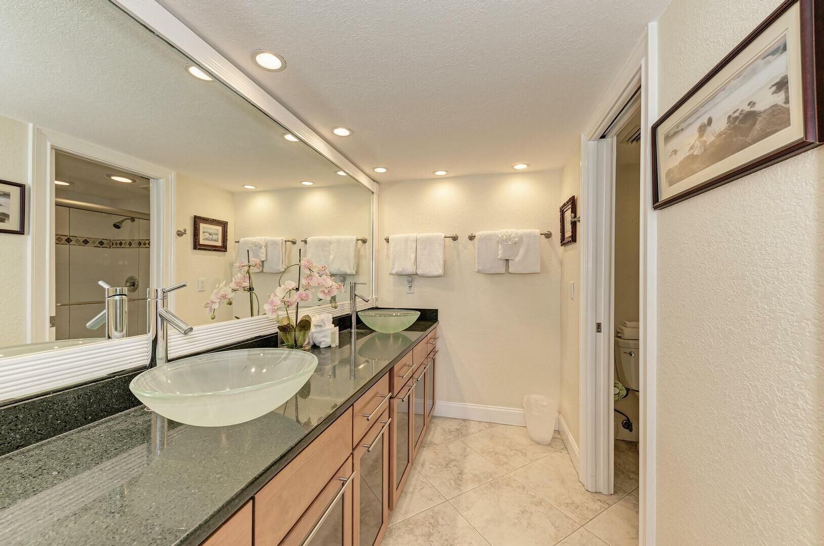 A modern bathroom with a large glass sink, two mirrors, a vanity with drawers, and a shower area visible through a glass door.
