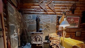 Interior rústico de uma cabana com parede de pedra, lareira a lenha, abajur e placa indicando proibição de fumar.