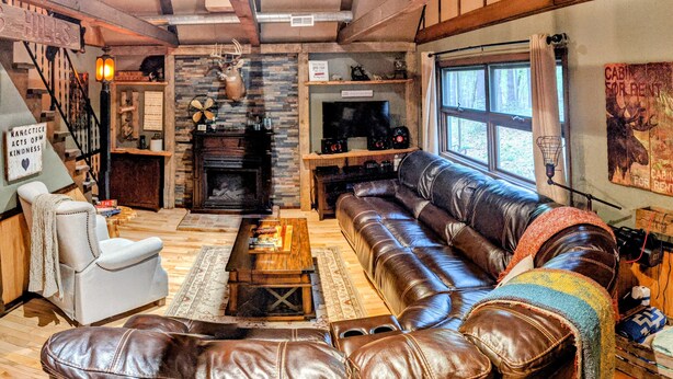 L’intérieur d’un chalet rustique, avec une cheminée en pierre, des meubles en cuir et un escalier en bois.