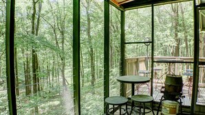 Une pièce dotée de grandes fenêtres donnant sur la forêt, de deux petites tables rondes et d’une bouteille de propane.
