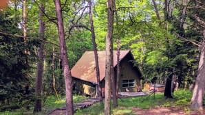 Un chalet rustique entouré d’une forêt dense, accessible par une rampe en bois.